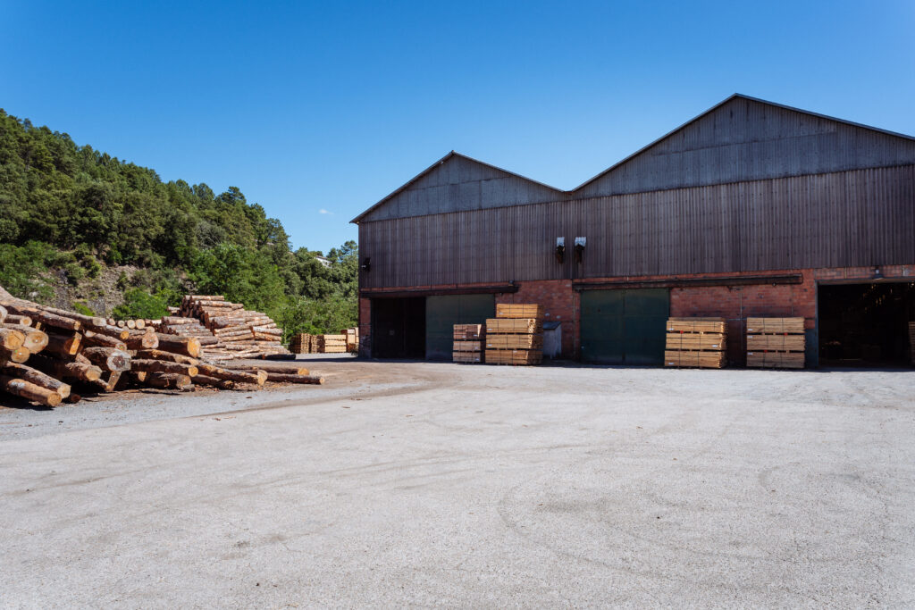 Intérieur d'un grand entrepôt avec de hautes piles de bois scié, éclairé par la lumière naturelle.